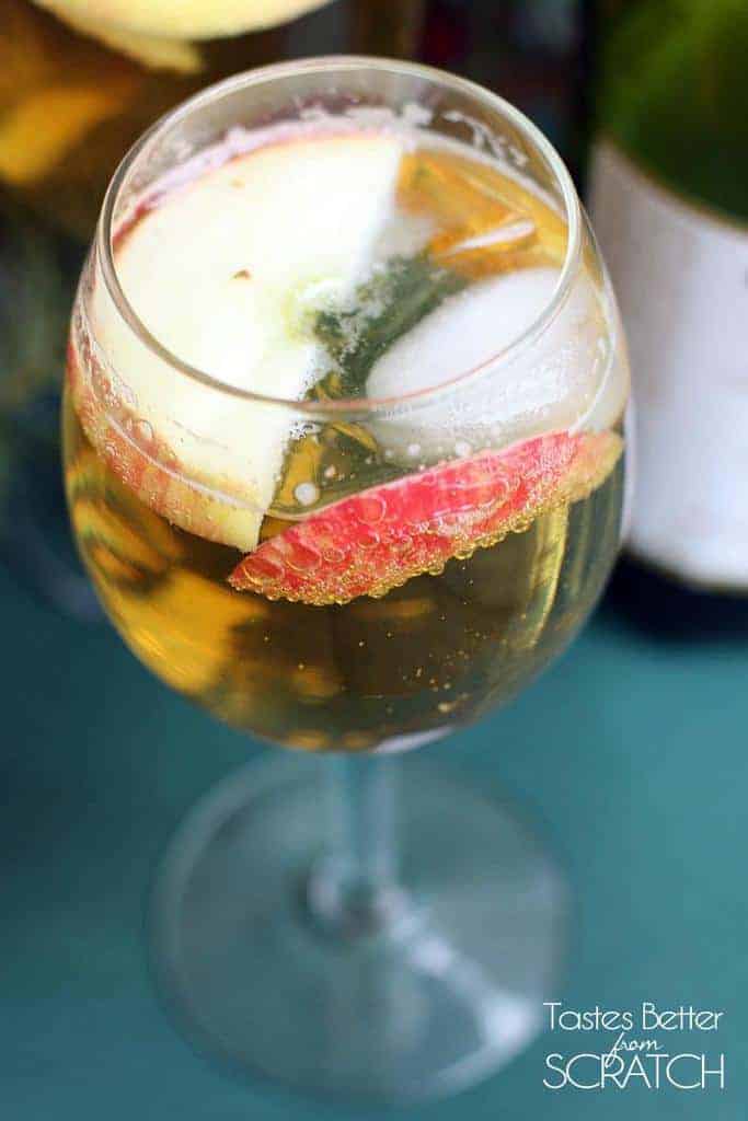 A clear glass filled with Homemade Sparkling Apple Cider (Martinelli's) with two apple slices.