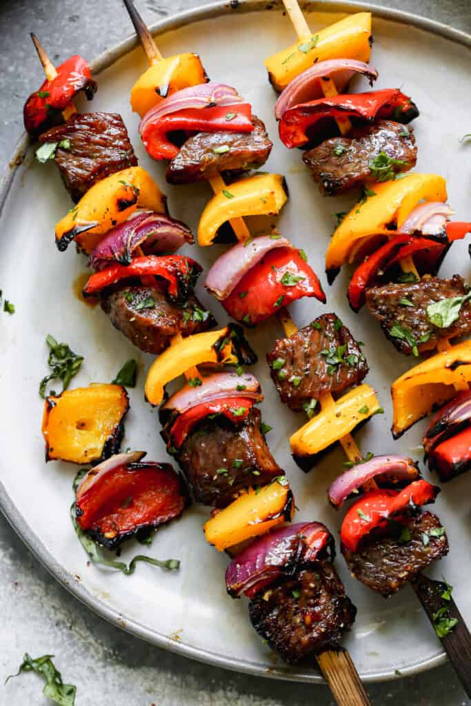 Three grilled steak kebob skewers on a plate.