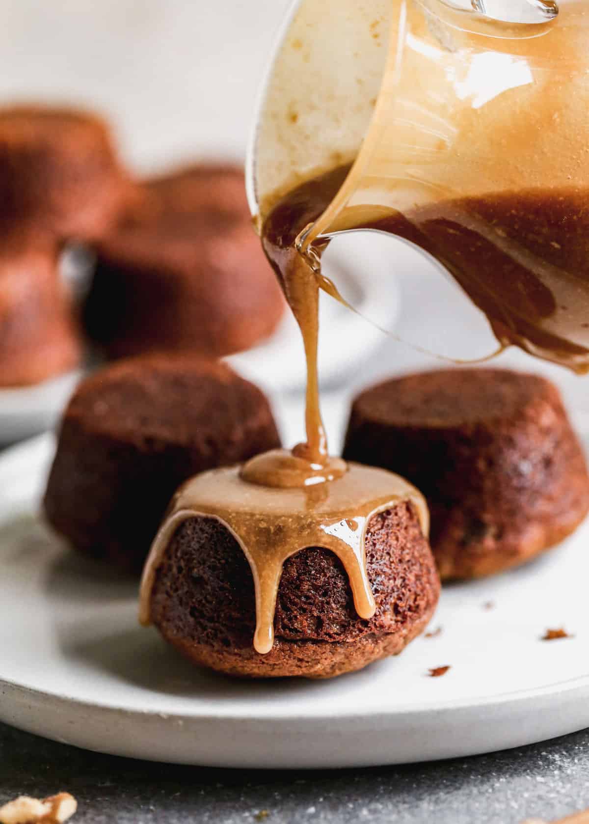 A homemade Toffee Sauce being poured on top of a single sticky toffee pudding. 