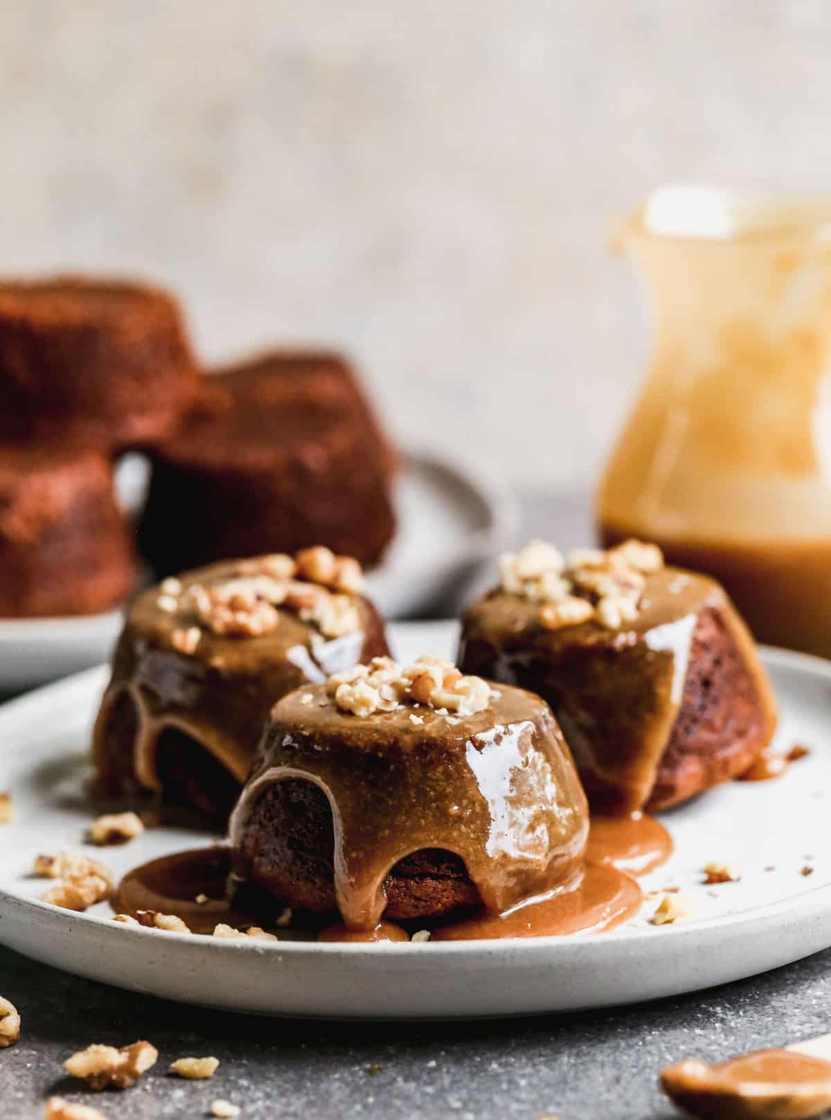 Three single serve Sticky Toffee Pudding on a plate topped with a caramel toffee sauce.