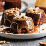 Three single serve Sticky Toffee Pudding on a plate topped with a caramel toffee sauce.