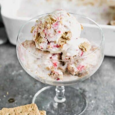 Three scoops of homemade strawberry cheesecake ice cream in a tall glass.