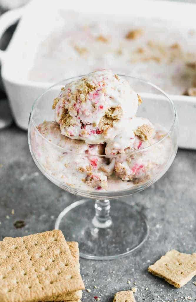 Three scoops of homemade strawberry cheesecake ice cream in a tall glass.