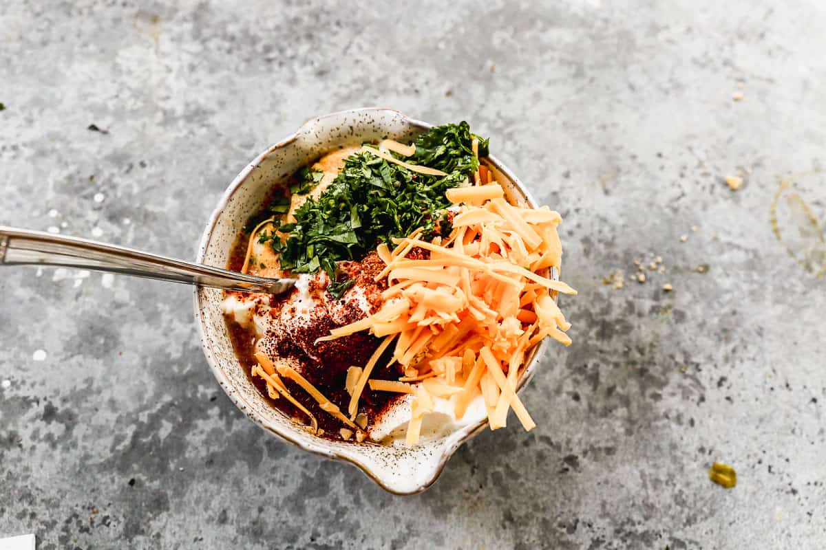 A small bowl filled with mayonnaise, yogurt, chili powder, tajin, garlic powder, cilantro, lime juice, and cheddar cheese to make a Street Corn Dip sauce.