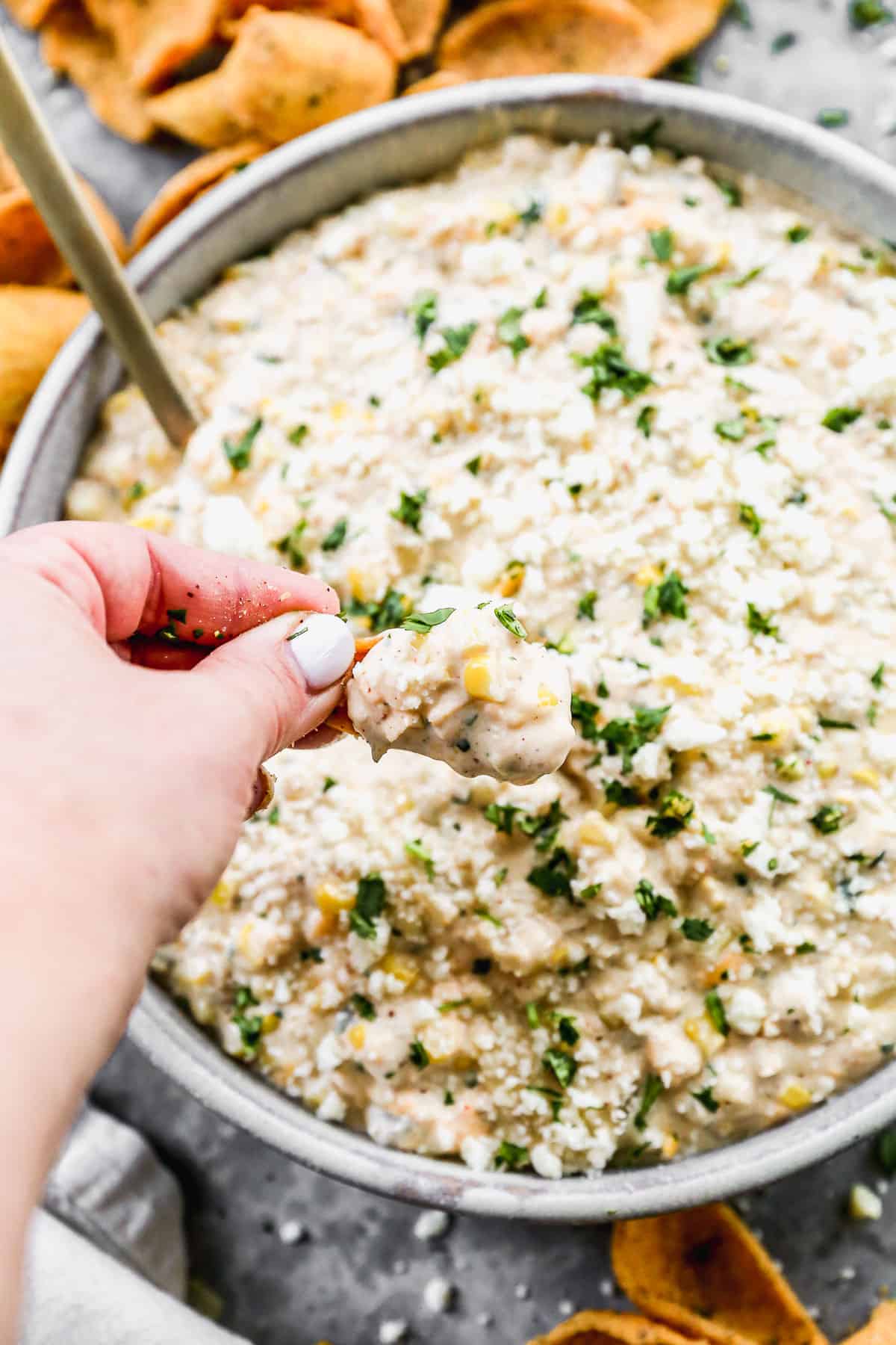 Someone scooping a frito chip into a bowl of Mexican Street Corn Dip. 