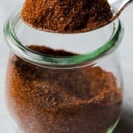 A spice container with homemade taco seasoning lifted out by a spoon.