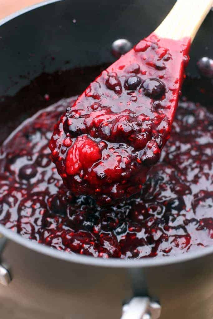 A saucepan full of homemade berry pie filling with a wooden spoon in it.