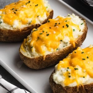 Three Twice Baked potatoes topped with melted cheddar cheese and chives, on a white plate.