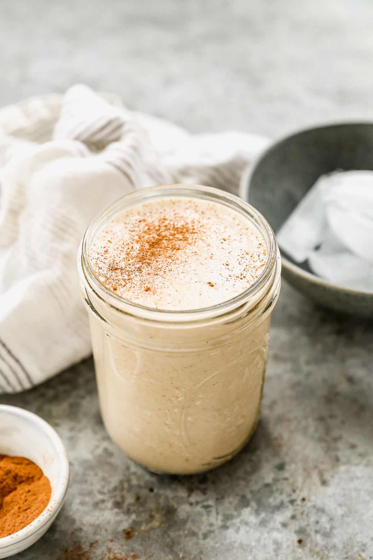 A mason jar filled with a Vanilla Protein Shake recipe and dusted with cinnamon. 