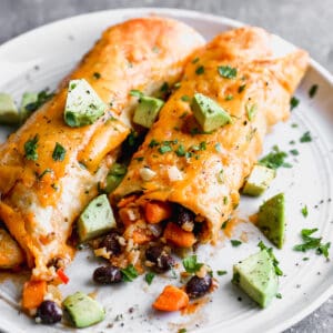 Easy Vegetarian Enchiladas on a plate topped with fresh avocado, ready to enjoy.