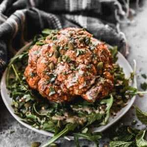 A whole head of Roasted Cauliflower on a plate of arugula, ready to cut and serve.