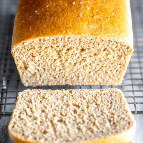 Whole wheat bread on a wire cooling rack with two slices cut from it.