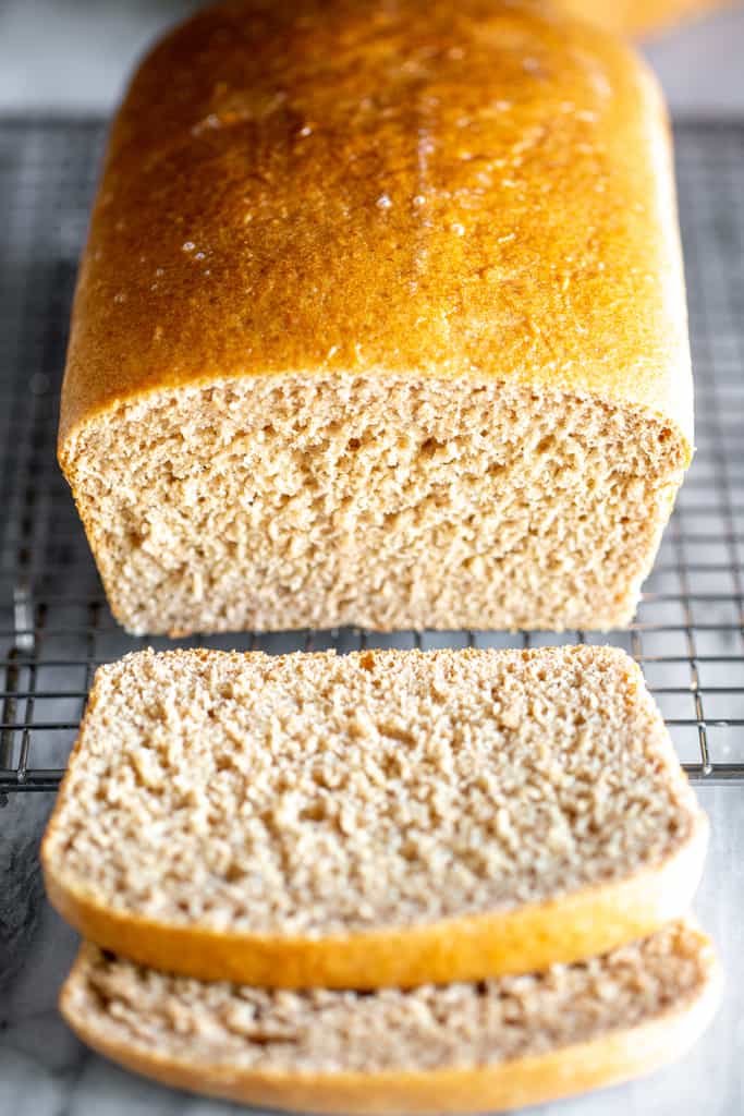 Whole wheat bread on a wire cooling rack with two slices cut from it.